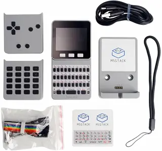 Image showing the M5Stack Faces kit arranged on a white background. Top left: a gray gamepad with a directional pad and four buttons. Center top: a small handheld computer with a screen and keyboard. Top right: a coiled black cable. Left side: a gray calculator keypad. Right side: a wall mount with white M5STACK logo. Bottom left: a clear plastic bag of colorful jumper wires. Bottom center: M5STACK stickers including replacement labels for the keyboard. Bottom right: a black lanyard attachment.